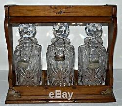 An Edwardian Oak Three Bottle Tantalus with 3 Metal Decanter Labels